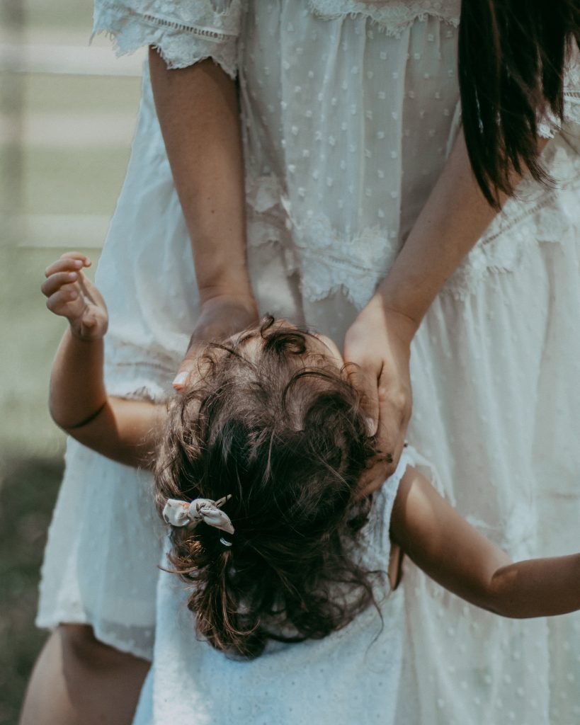 mom holding little girls face with curly hair and hairbow mama in white dress